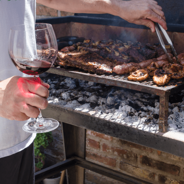 Man grilling meat meat while drinking Argentine wine