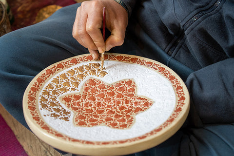 Kashmiri Naqashi artisan painting traditional chimar design in relief style on a Papier mache plate.
