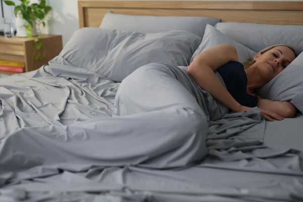 person smiling in their sleep in bed, covered in the evercool cooling comforter and matching evercool cooling sheet set in cool grey