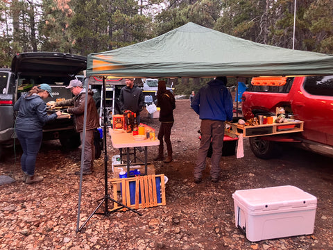 A pop up tent shelters folks from the rain as they cook on a Thunderbolt Adventure Supply Camp Kitchen