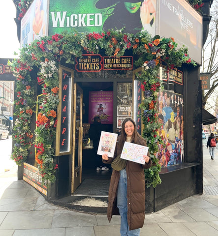 London artist stood outside the Theatre Cafe Merchandise Shop down Shaftesbury Avenue, holding up some art prints of West End Theatres.