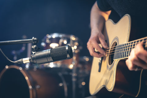 male musician playing acoustic guitar behind microphone