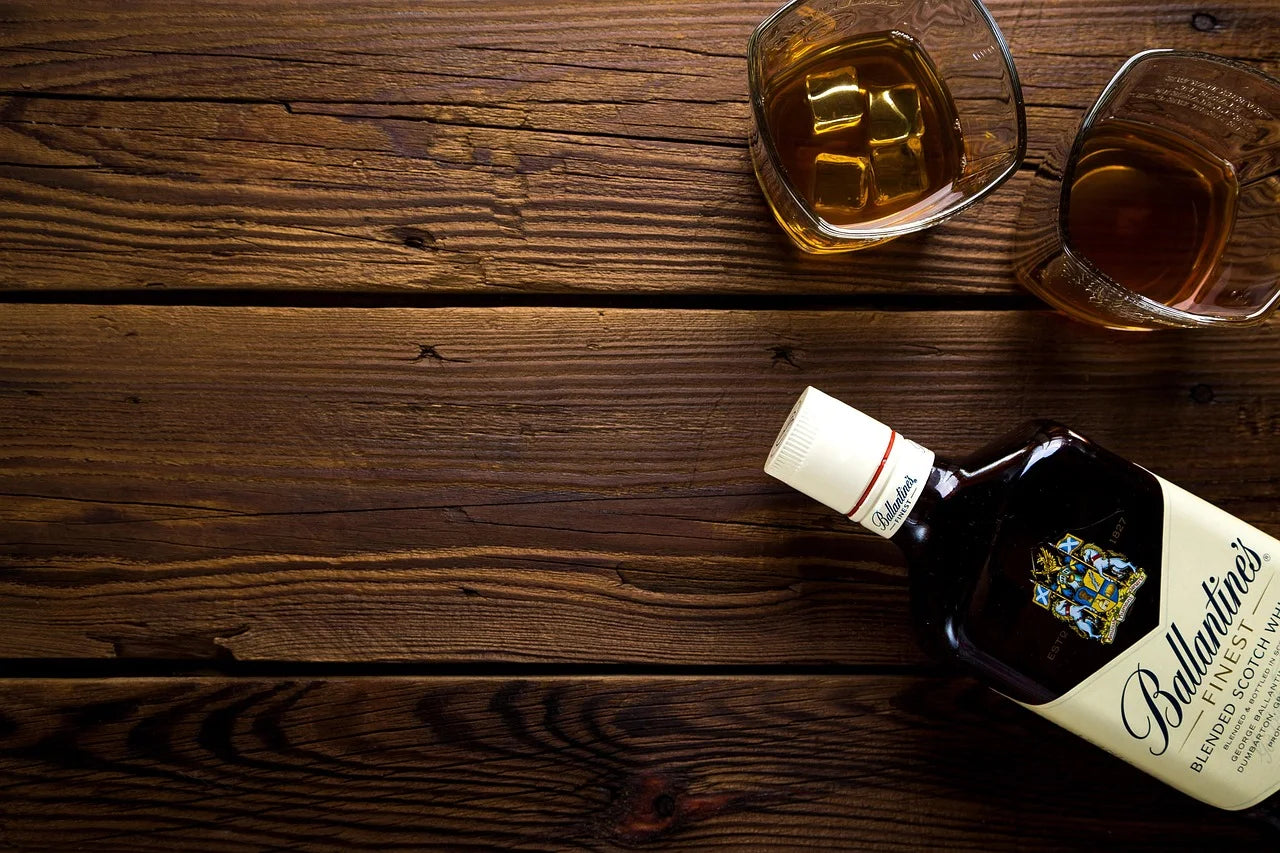 Deux verres et une bouteille de whisky "Ballantines" posés sur une table en bois