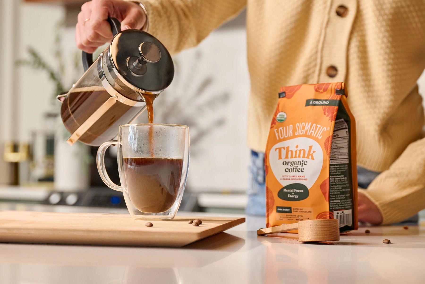 Person pouring coffee from French press into mug next to a bag of organic coffee.