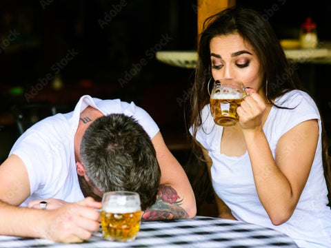 man passed out at bar table next to a woman drinking her beer