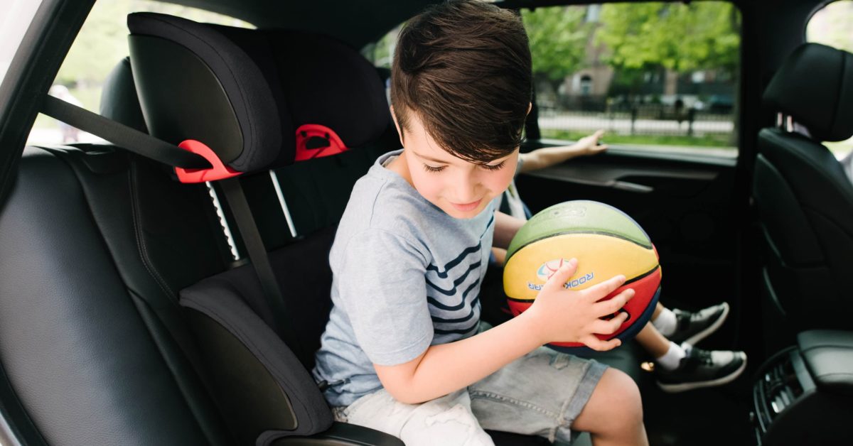 Boy getting out of his Clek Oobr booster seat to play basketball