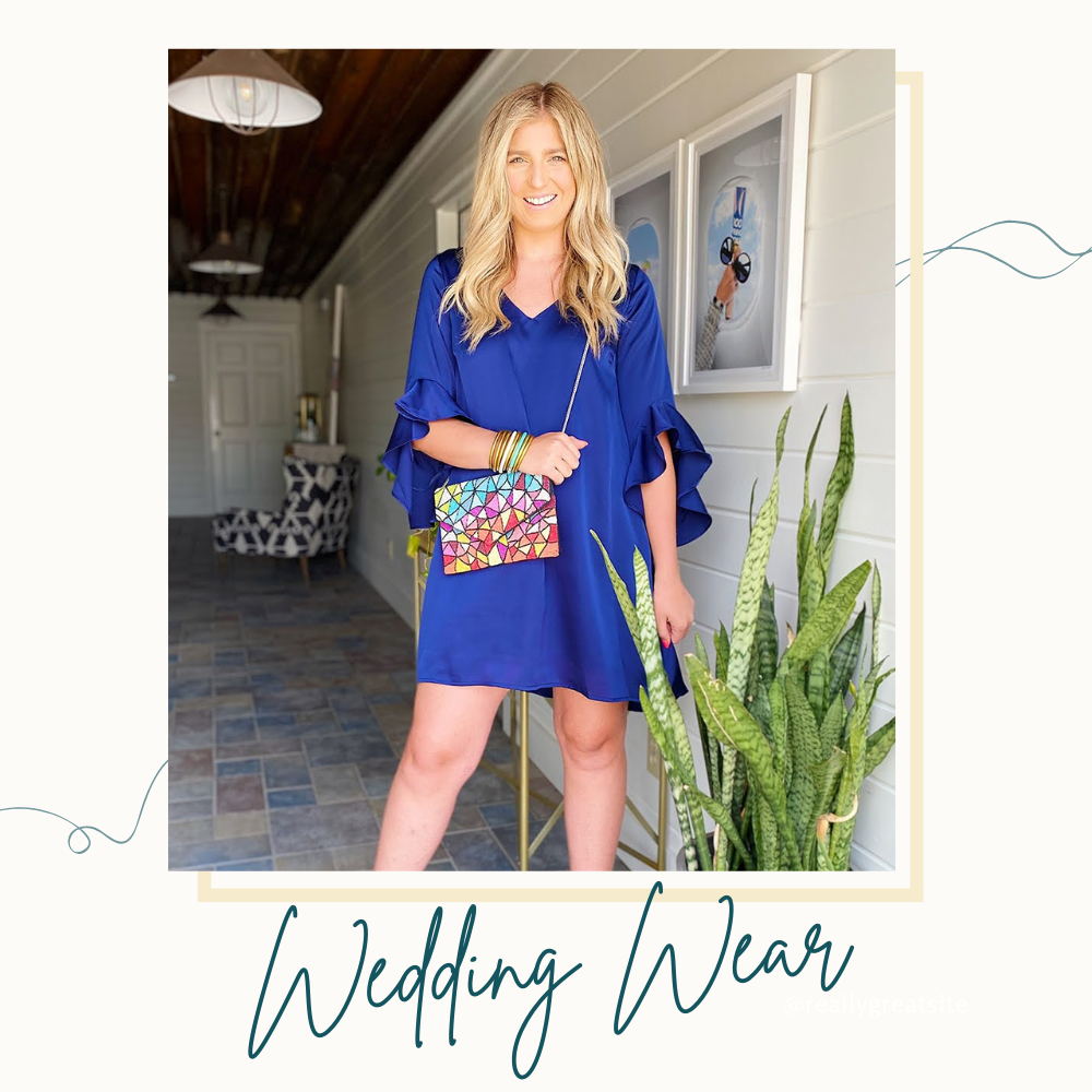 Wedding Wear Collection: Model wearing a navy satin dress with cascading ruffle detail on the three-quarter sleeves paired with a multicolor beaded clutch