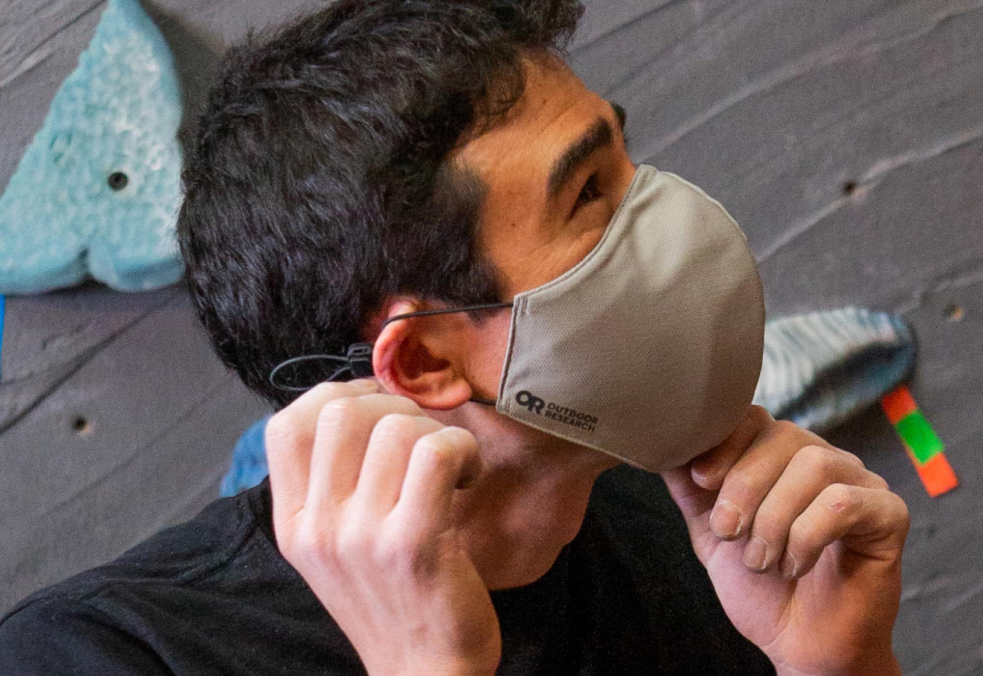 Keenan Takahashi adjusts the fit of the Outdoor Research Essential Face Mask before attempting an indoor boulder problem.