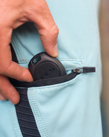 FCS Sharkbanz Pod being attached to the key tie on a surfer's boardshorts