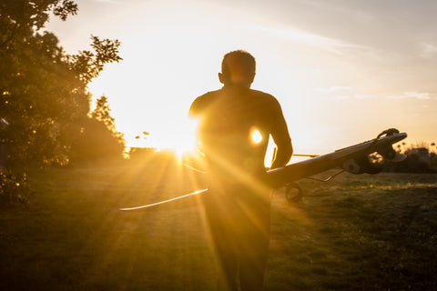 Surfer carrying surfboard with sun glaring in background in New Zealand