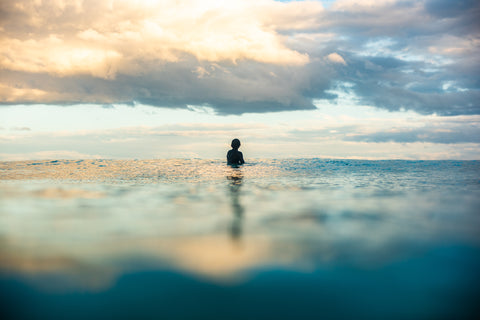 Lone surfer sitting in blue sea with clouds overhead at Wainui Beach in Gisborne, NZ