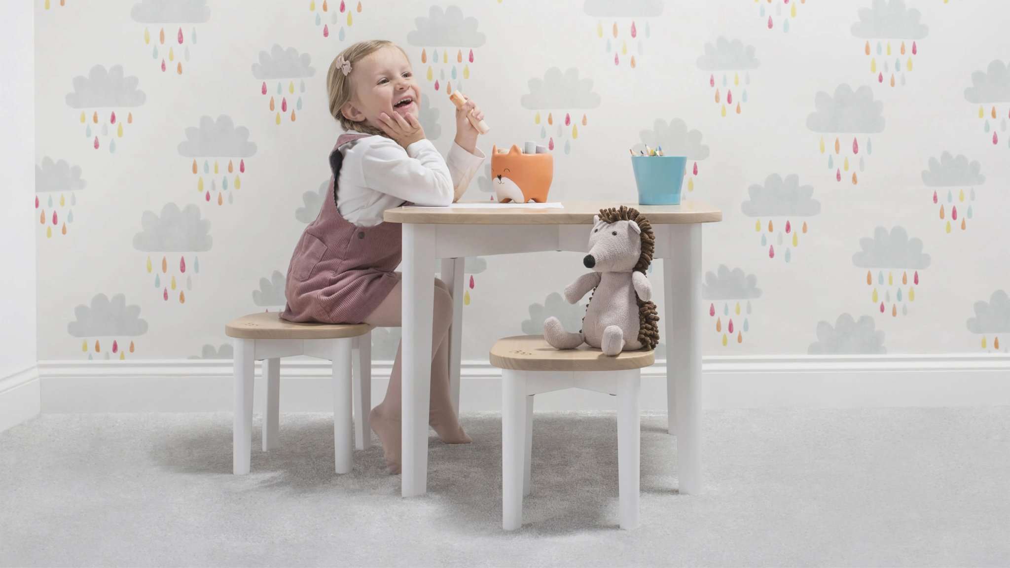 girl sits at play table with cuddly toy on stool