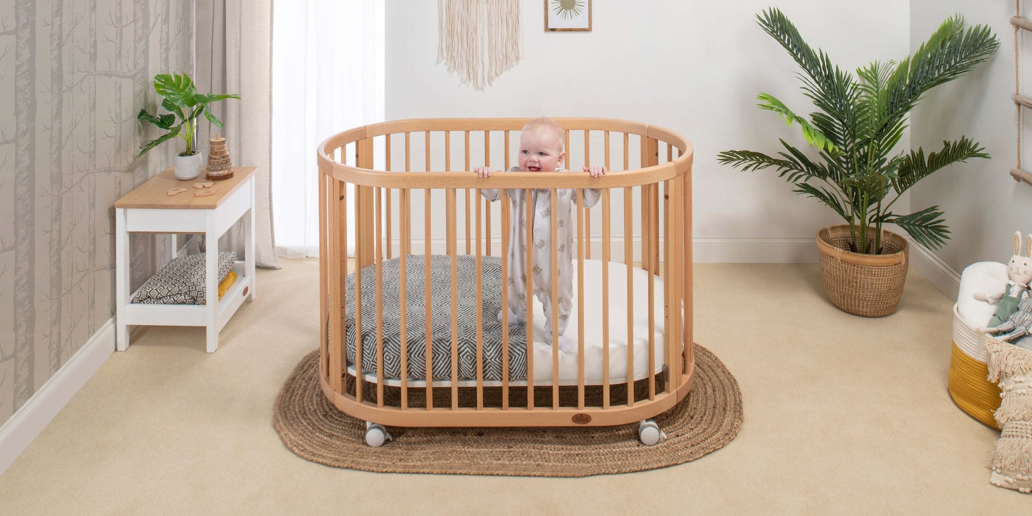 wooden oval cot with baby peeking over the bars