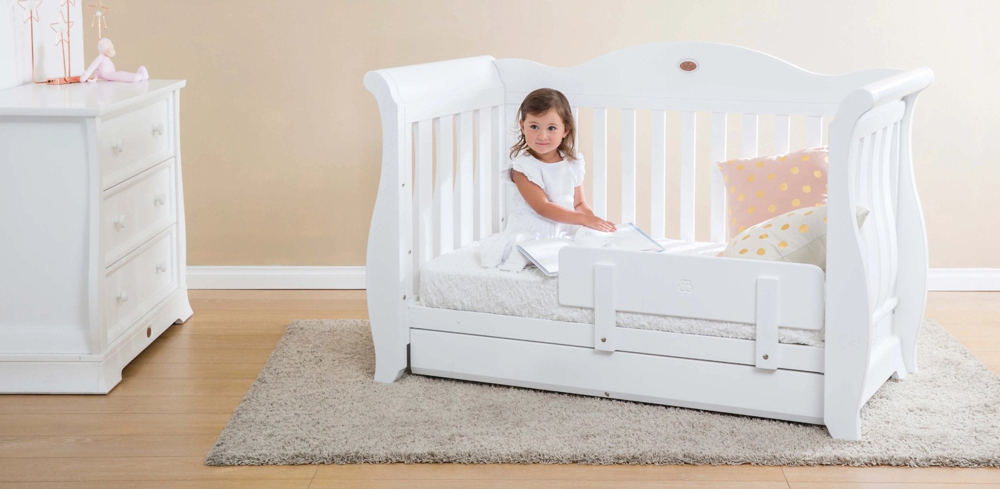 toddler girl sits in sleigh bed with toddler guard panel