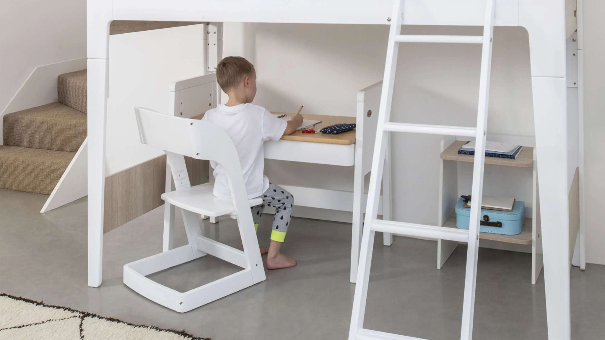 child works at desk positioned under loft bed