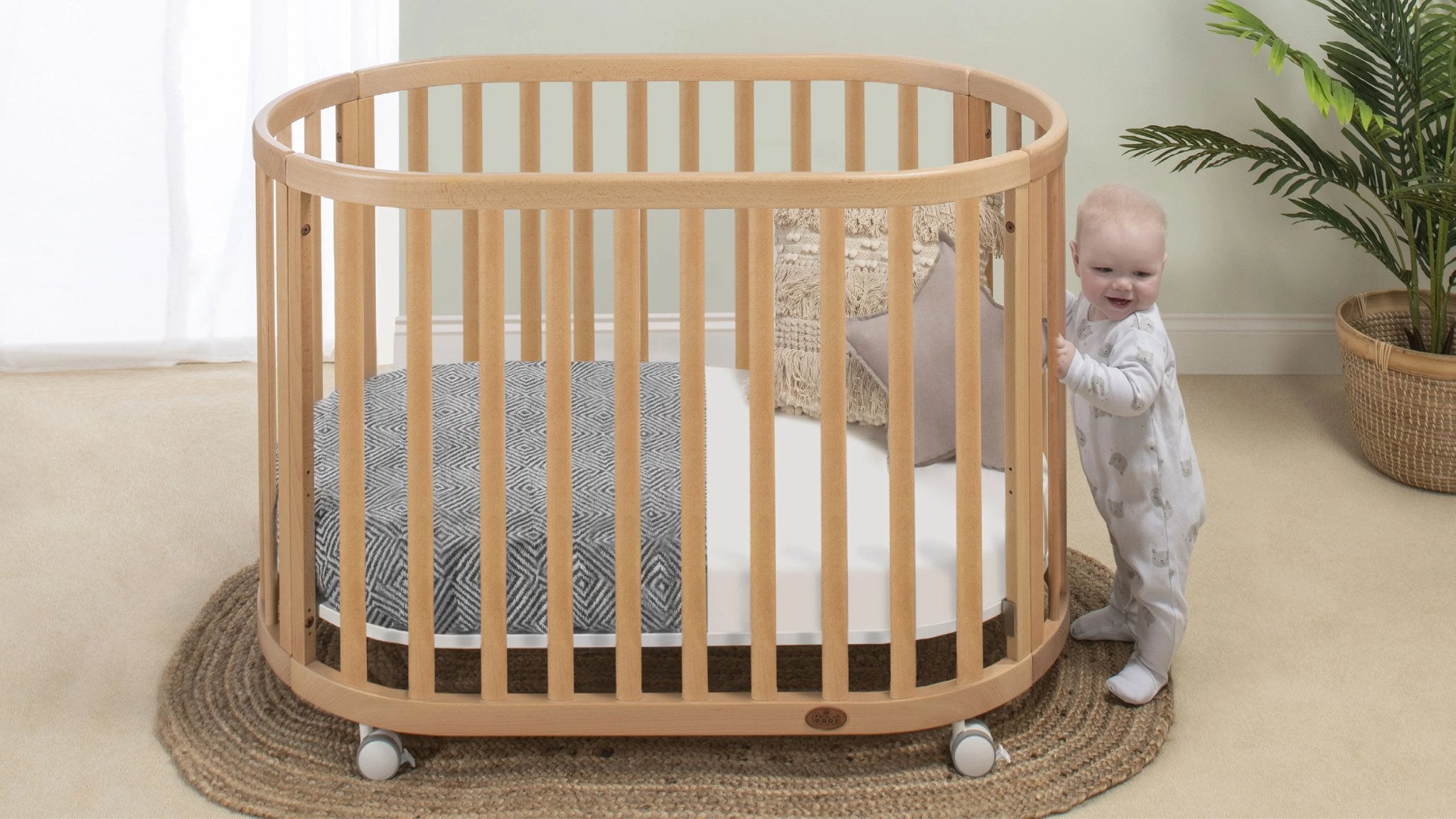 baby holds onto side of wooden oval cot