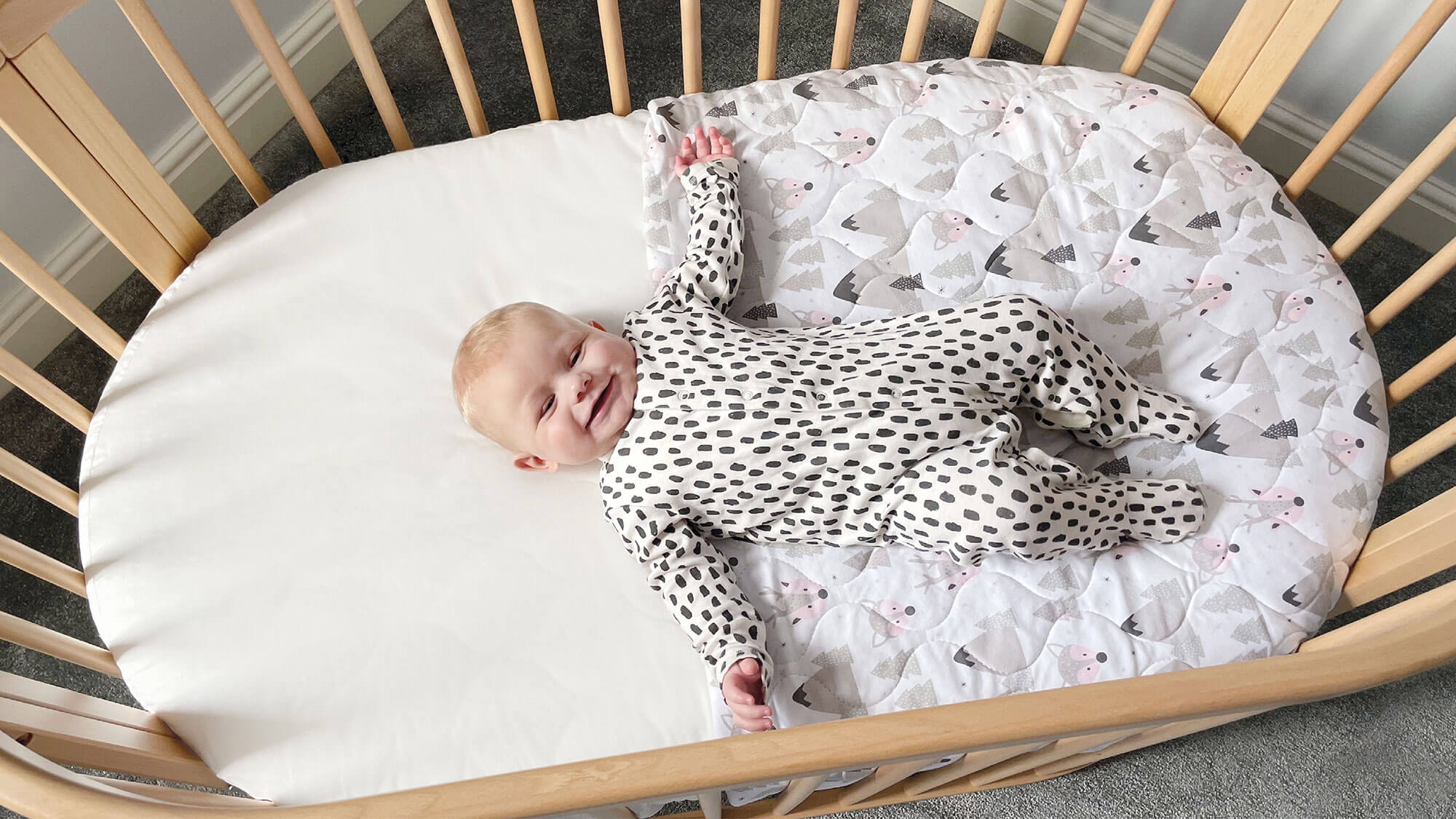 Baby laughing lying down in oval cot