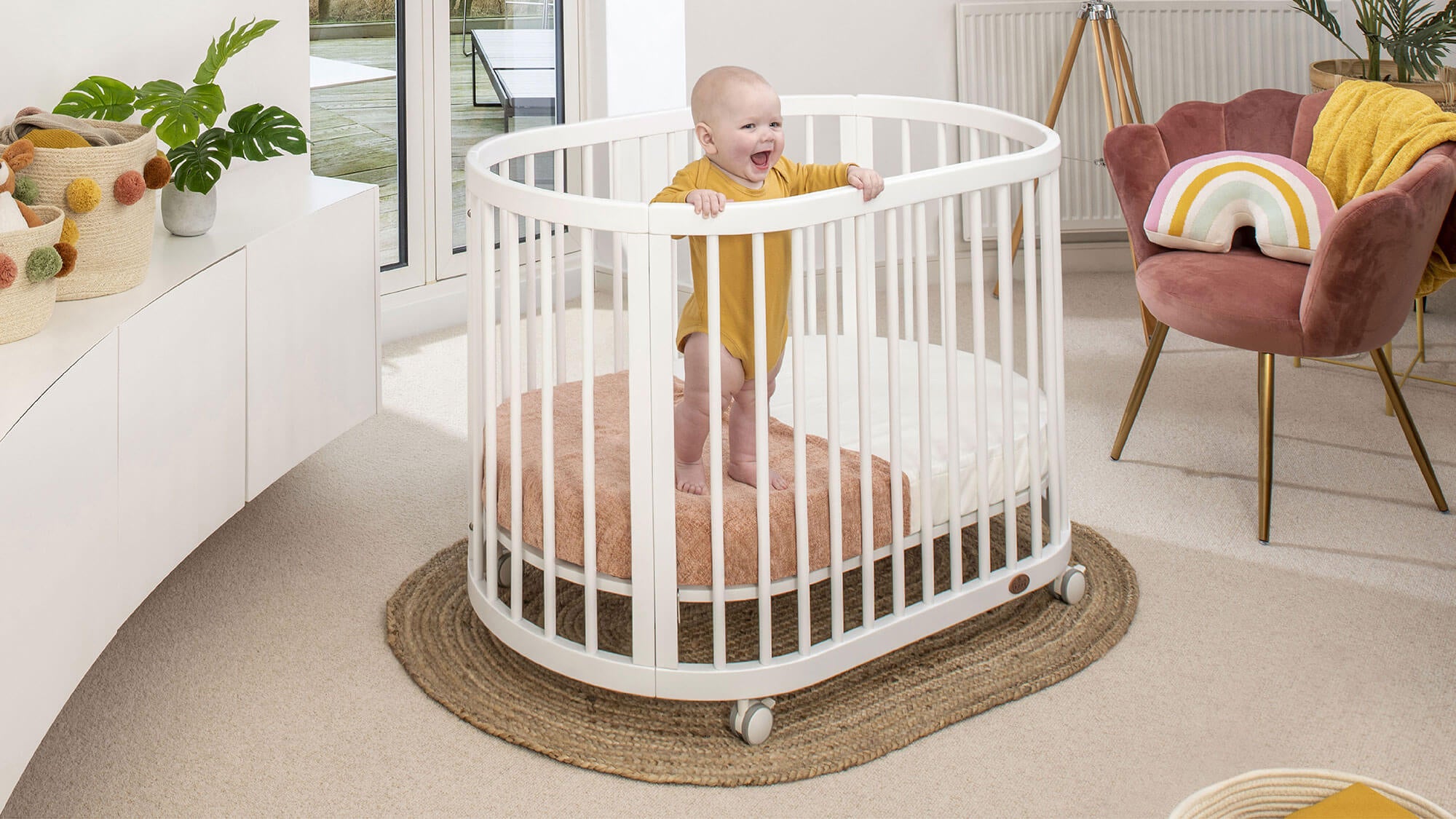 Baby standing and laughing in oval cot
