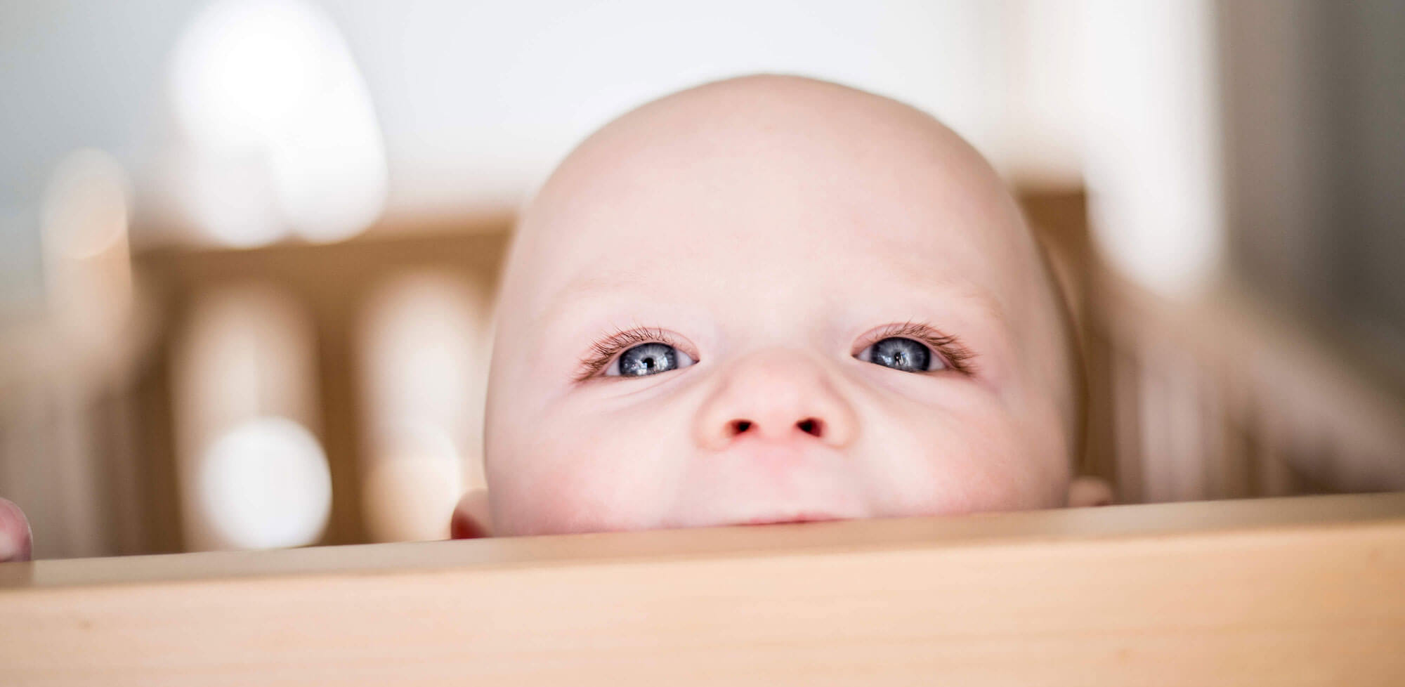 Close-up of baby peeking over side of cot