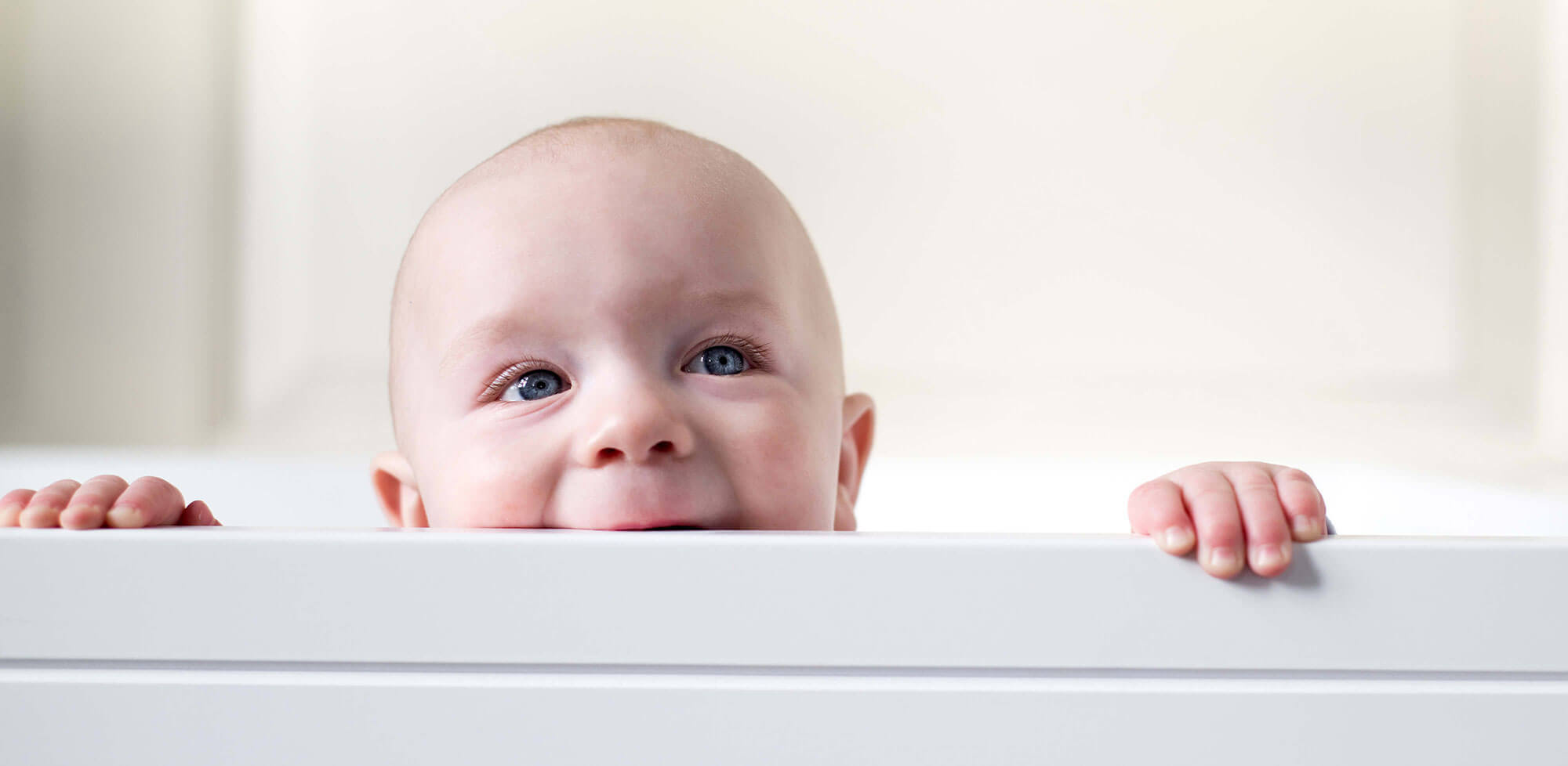 Baby peeking over side of cot