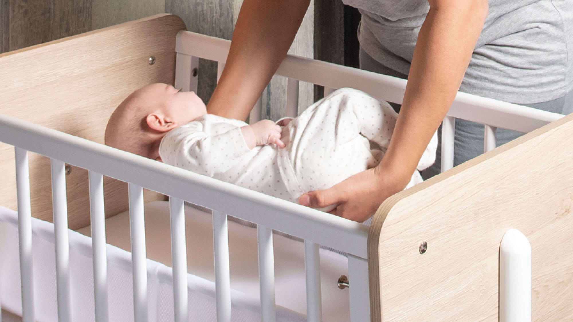 Mum lifting baby into bedside crib