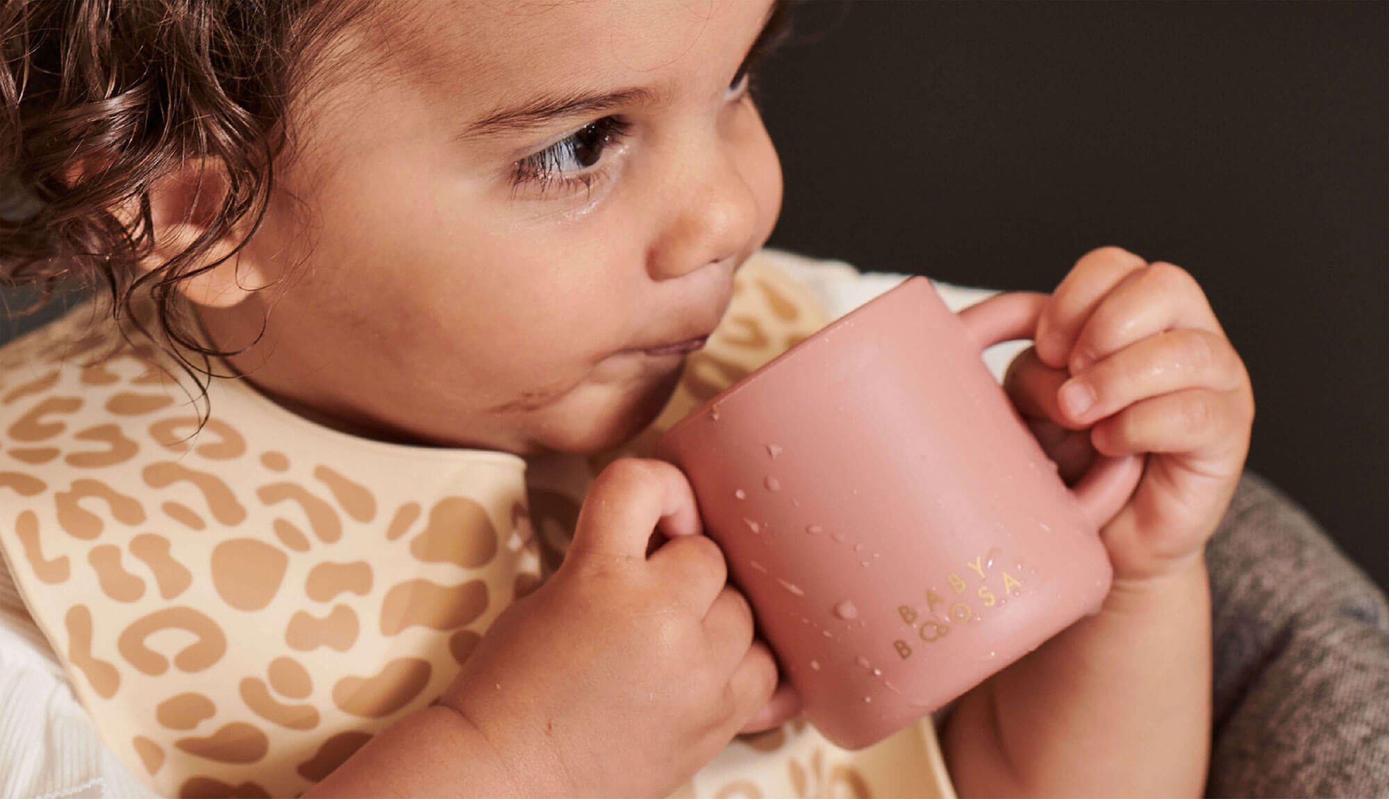 Toddler holding a pink open cup by two side handles