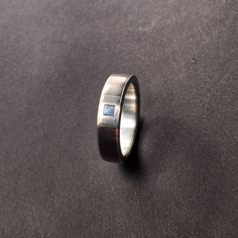 A square inlay of fine silver and labradorite handsomely embellishes this 5mm titanium band with fine silver sleeve. Size 7.