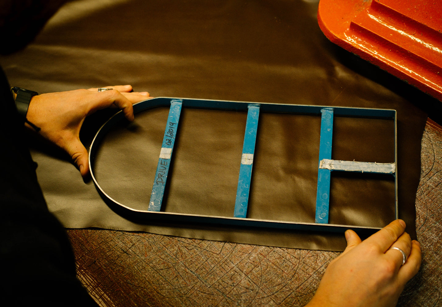 Photo of a craftsperson layout a metal pattern on a piece of cut leather