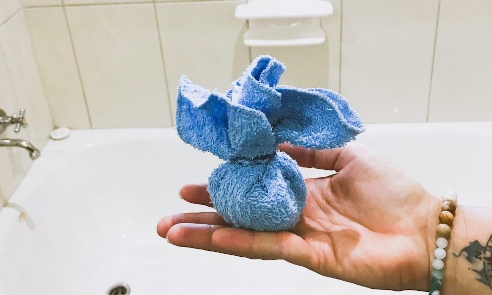 and holding blue face washer containing coffee grounds thats tied up in a ball over a bathtub