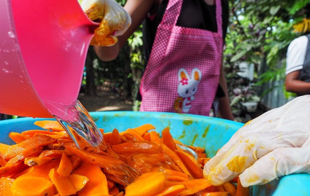 woman in pink apron pouring water over sliced turmeric in a bucket in timor-leste