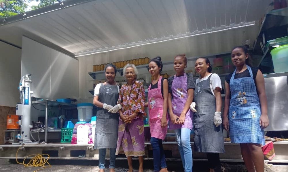 six smiling timorese women standing in front of shipping container preserving kitchen