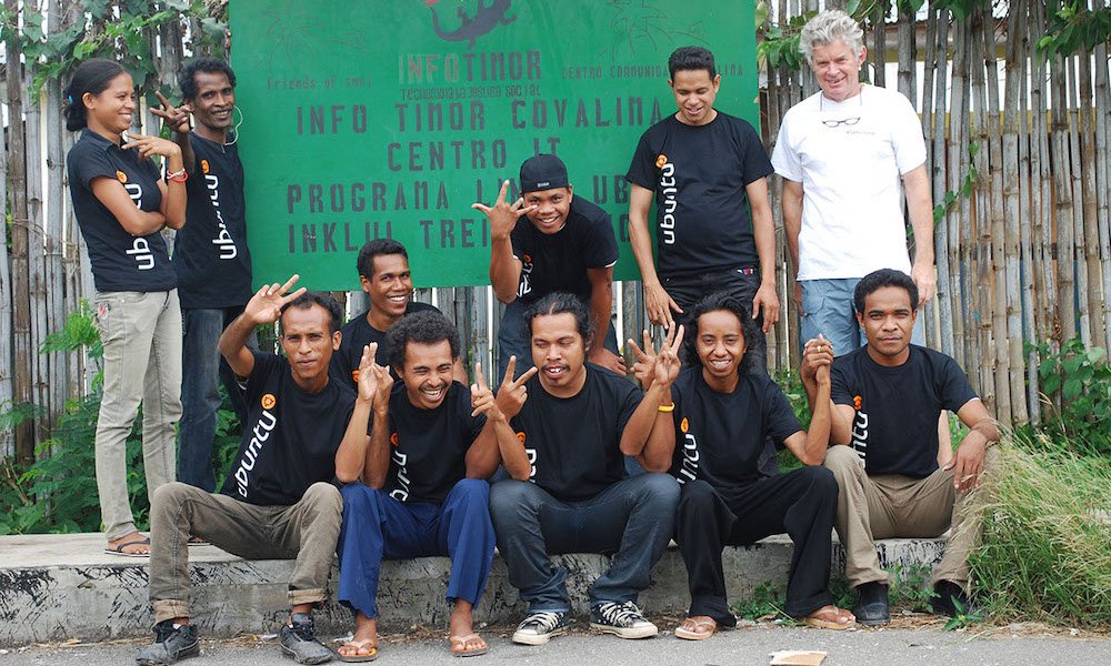 group of people in timor-lests wearing black shirts saying ubuntu as they laugh and do peace fingers