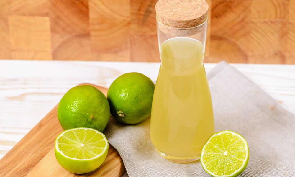 lime cordial bottle sitting on chopping board next to chopped limes