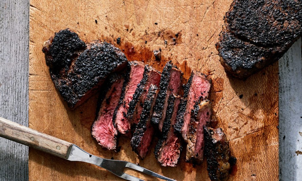 piece of rare cooked steak with coffee grounds rub sitting charred and sliced on a chopping board