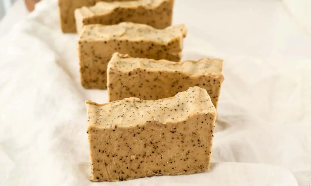 bars of beige handmade coffee soap speckled with coffee grounds sitting on white tissue paper