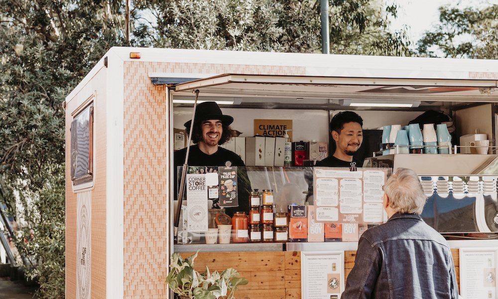 two baristas in coffee van at melbourne farmers market smiling at customer