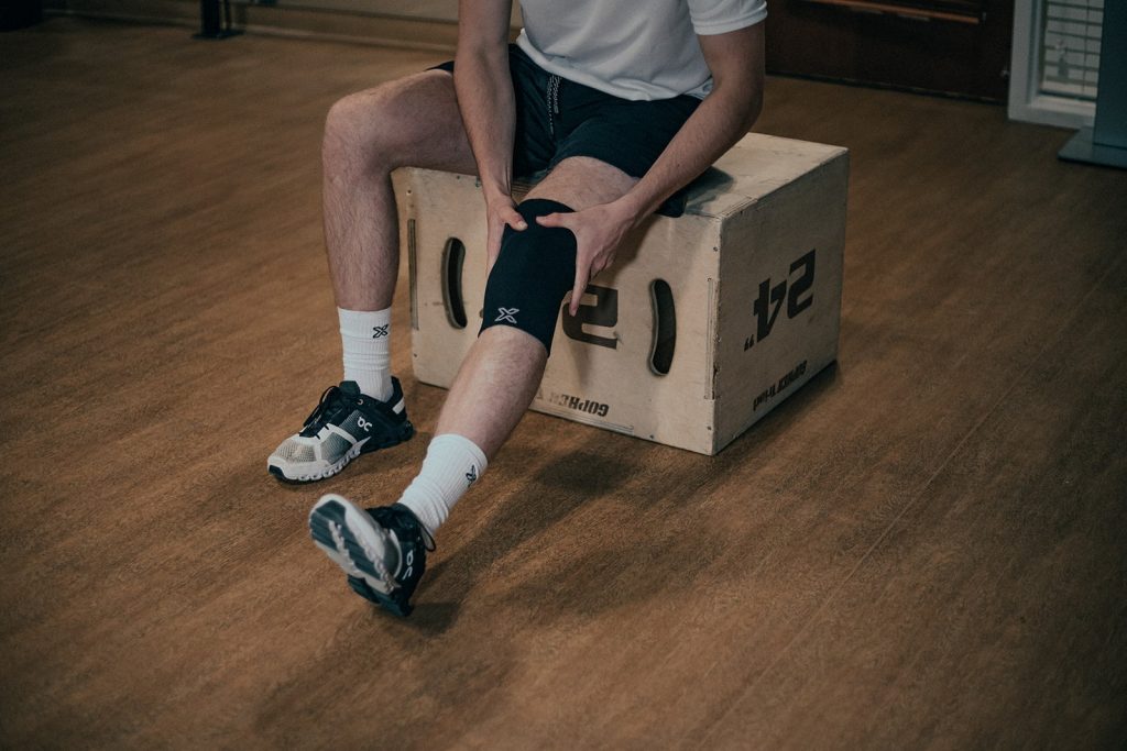 man on a crate wearing a body helix knee compression sleeve for his knee injuries