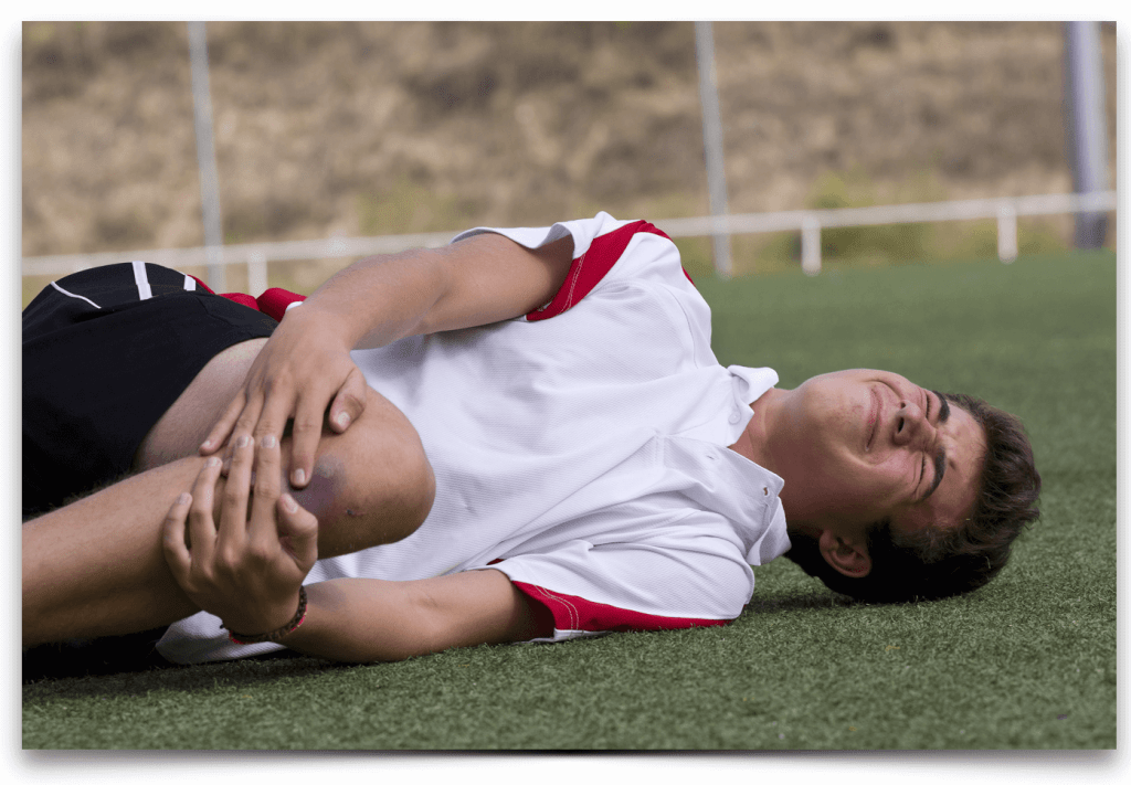 youth on a soccer field holding his leg, with knee pain and injury