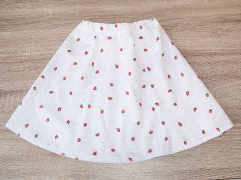 A girl's white summer skirt with little red strawberries and hearts laid out on table
