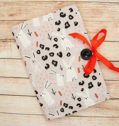 A notepad with a fabric covering made from beige rabbit printed fabric with an orange ribbon
