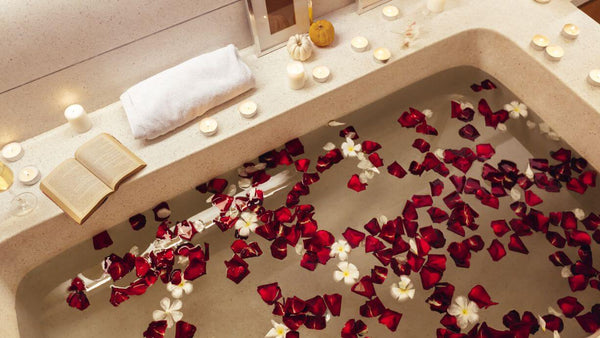 a bathtub with rose petals in it and candles and a book on the side