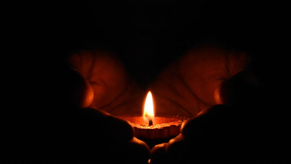 a person holding their hands together to create a heart shape in front of a candle