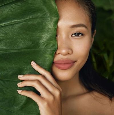 Picture of woman with beautiful glowing skin in a natural setting with large green leaf, for our blog post on Anti Aging Skin Restoration.