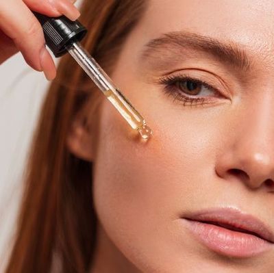 a woman applying facial serum to her cheek using a dropper, for our blog post on Best Serums for Acne Prone Skin.