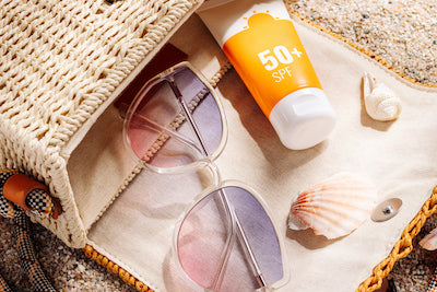 A purse on its side at the beach with sunglasses, seashells and sunscreen