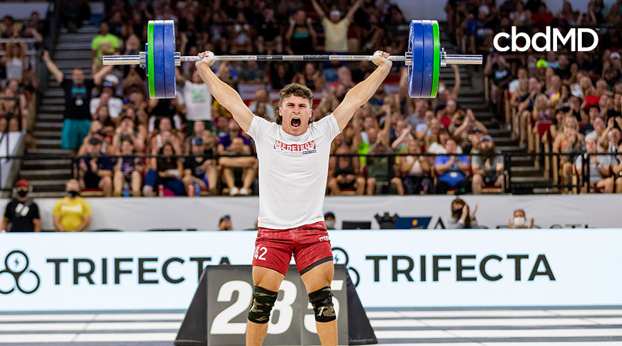 Justin Medeiros holding a barbell with weights above his head in front of a crowd