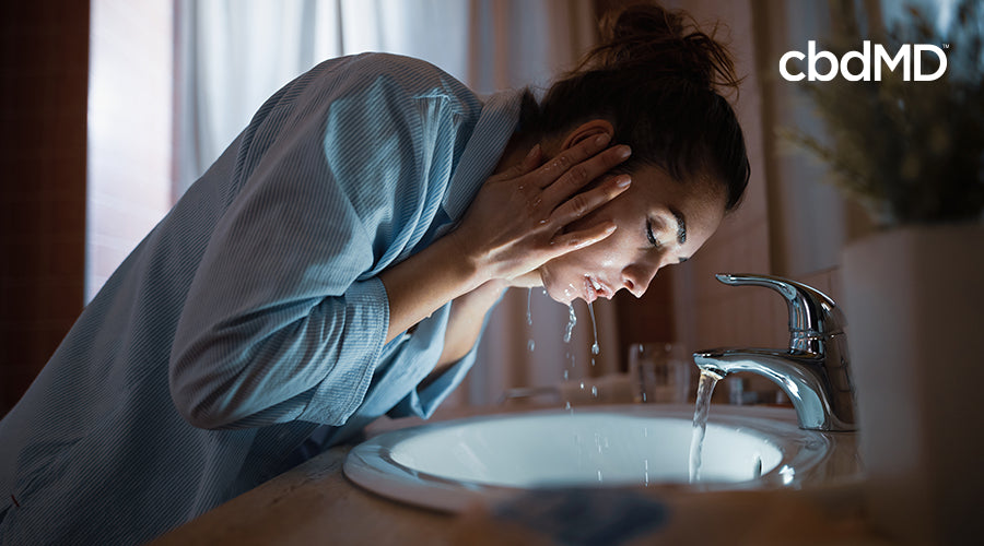 An attractive woman getting
    ready for bed washes her face over a sink