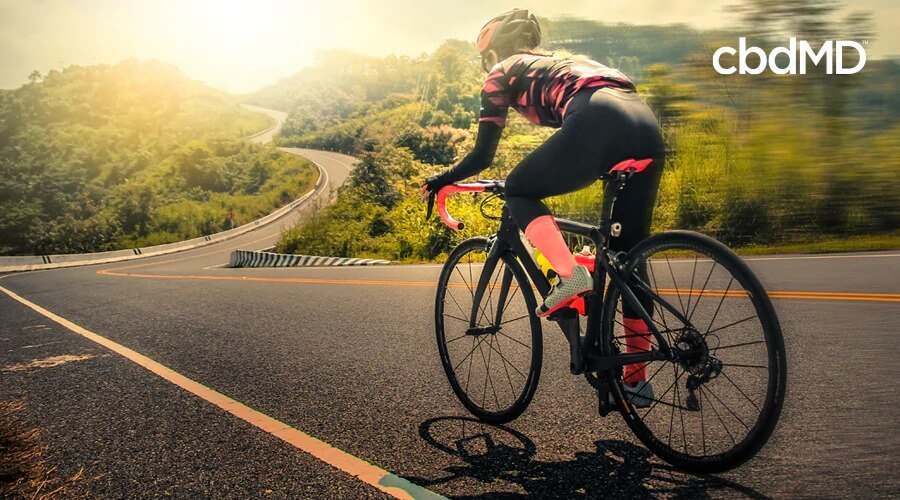 Uma mulher vestida com equipamento de montaria preto e rosa anda de bicicleta por uma estrada larga e sinuosa