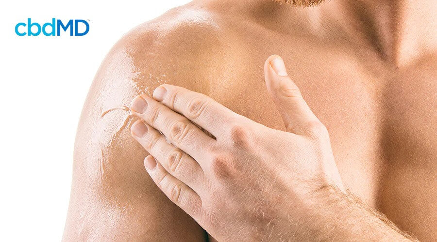 A close up of a shirtless man rubbing cbd oil on his shoulder