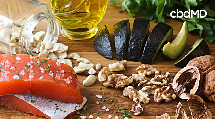 An assortment of healthy food that includes salmon, avocado, walnuts, and oils sits all together